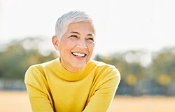 Senior woman in a yellow shirt sitting outside smiling