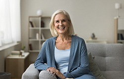Senior woman smiling and sitting on a grey couch