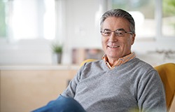 Senior man with glasses sitting back in chair and smiling