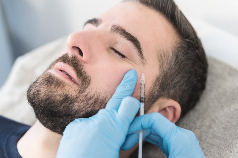 a young man with a dark beard and his eyes closed receiving a BOTOX injection