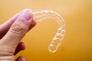 Person holding up a clear aligner in front of a yellow background