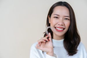 Woman smiling while holding an Invisalign clear aligner
