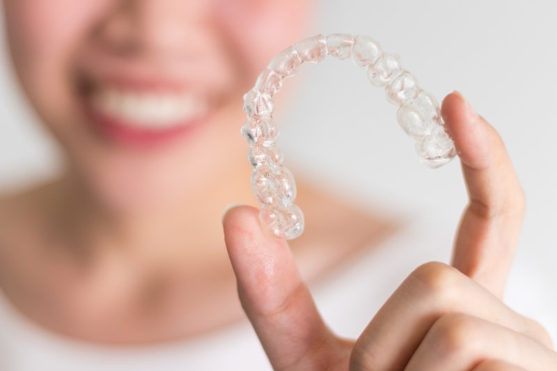 smiling woman holding Invisalign aligner