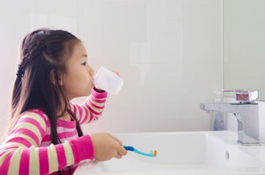 Young child rinsing her mouth after brushing her teeth.
