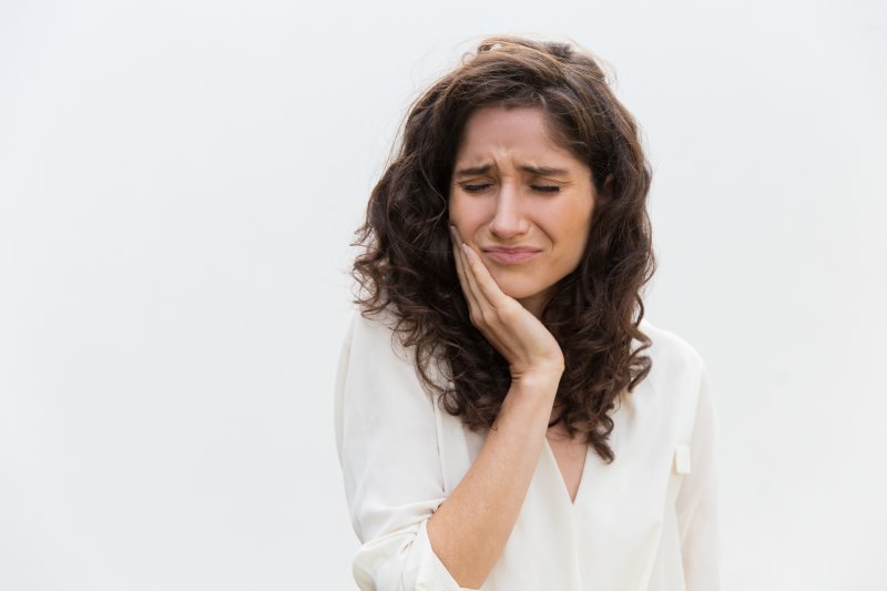 Woman holds cheek in pain.