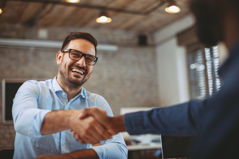 A man shaking hands with a prospective employer, smiling after his cosmetic dentistry